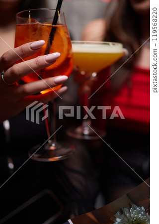 A woman holds a cocktail in her hand, with her fingers wrapped around the glass 119568220