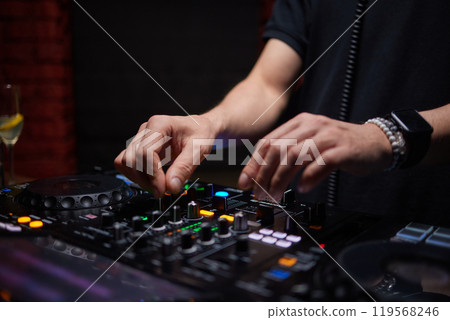control DJ for mixing music with blurred people dancing at party in nightclub. 119568246