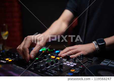 control DJ for mixing music with blurred people dancing at party in nightclub. 119568247