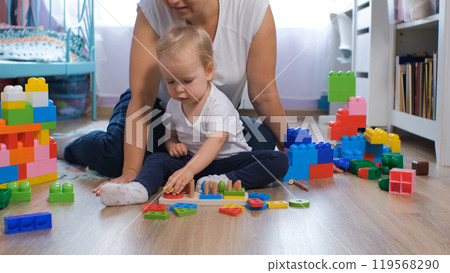 Loving mother and baby daughter play together with colorful wooden toys in their cozy nursery at home 119568290