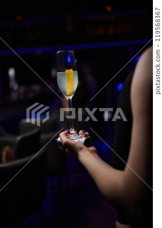 A woman holds a cocktail in her hand, with her fingers wrapped around the glass A woman holds a cocktail in her hand, with her fingers wrapped around the glass 119568367