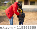 Mother helping baby keeping warm wearing warm clothes standing outdoors. 119568369