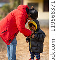 Mother helping baby keeping warm wearing warm clothes standing outdoors. 119568371