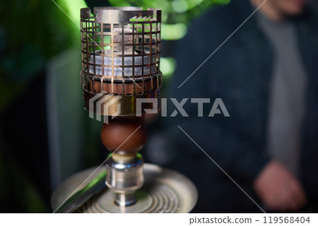 Close up of a hookah made of metal and glass on a wooden table 119568404
