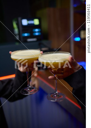 A woman holds a cocktail in her hand, with her fingers wrapped around the glass A woman holds a cocktail in her hand, with her fingers wrapped around the glass 119568411