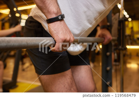 A man is strengthening and improving his fitness by lifting a barbell in the gym A man is strengthening and improving his fitness by lifting a barbell in the gym 119568479