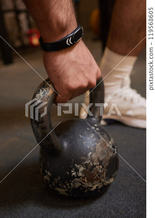 Man is performing a workout in the gym by lifting a kettlebell, focusing on strength and endurance Man is performing a workout in the gym by lifting a kettlebell, focusing on strength and endurance 119568605
