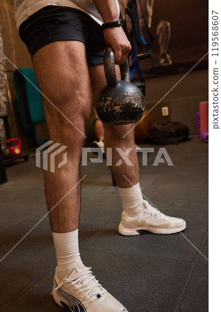 Man is performing a workout in the gym by lifting a kettlebell, focusing on strength and endurance Man is performing a workout in the gym by lifting a kettlebell, focusing on strength and endurance 119568607