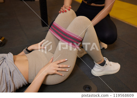 Woman working out with a resistance band under the guidance of her trainer in a gym setting 119568609