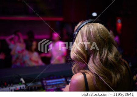 control DJ for mixing music with blurred people dancing at party in nightclub. 119568641