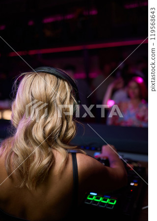 control DJ for mixing music with blurred people dancing at party in nightclub. 119568643