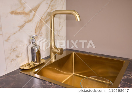 A gold faucet on a bathroom sink with a soap bottle A gold faucet on a bathroom sink with a soap bottle 119568647