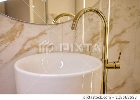 A gold faucet on a bathroom sink with a soap bottle A gold faucet on a bathroom sink with a soap bottle 119568658