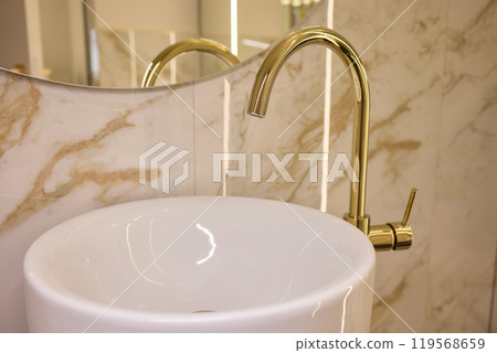 A gold faucet on a bathroom sink with a soap bottle A gold faucet on a bathroom sink with a soap bottle 119568659