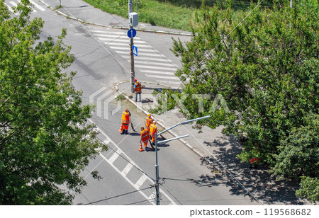 Municipal cleaners manually sweep the city roadway 119568682