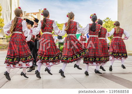Rear view of group of dancers wearing traditional folk dresses dancing on cultural festival 119568858