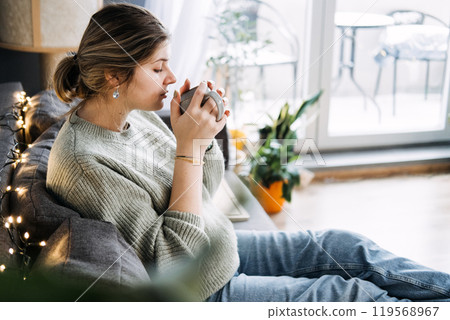 Pregnant woman enjoying a relaxing moment with a warm cup of tea, focusing on prenatal health and self-care. Cozy atmosphere with comfortable maternity wear. Pregnant woman enjoying a relaxing moment with a warm cup of tea, focusing on prenatal health and self-care. Cozy atmosphere with comfortable maternity wear. 119568967