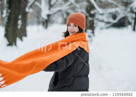 Woman in orange scarf and hat enjoying a snowy walk. Bold winter accessories, vibrant fashion, and colorful layering. Woman in orange scarf and hat enjoying a snowy walk. Bold winter accessories, vibrant fashion, and colorful layering. 119568982