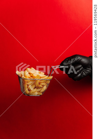 Crispy golden French fries in metal basket on a bold red background, perfect for fast-food promotion 119569428