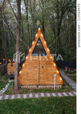 Cozy wooden A-frame cabins in forest with sunlight and outdoor seating area Cozy wooden A-frame cabins in forest with sunlight and outdoor seating area 119569470
