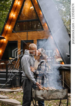 Romantic barbecue moment by the cabin, where love meets the smoky flavor of outdoor grilling 119569474