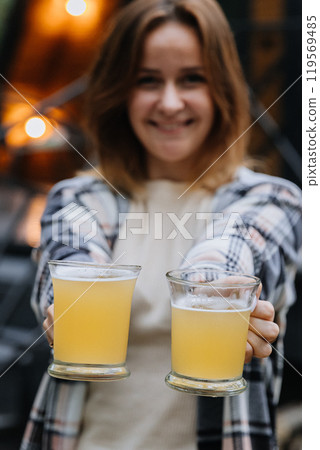 Woman offering two glasses of beer, smiling, inviting for toast, autumn gatherings outdoors 119569485