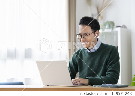 一名 30 多歲的男子戴著耳機坐在筆記型電腦前 119571248