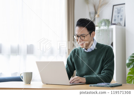 一名 30 多歲的男子在家使用筆記型電腦工作的照片 119571308