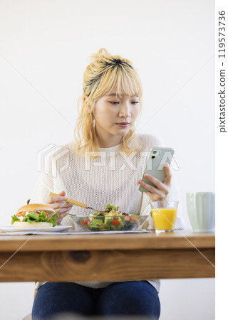 Woman eating breakfast while looking at smartphone 119573736