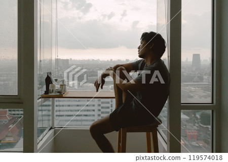 Introvert lonely man sitting hugging his knees looking out. 119574018
