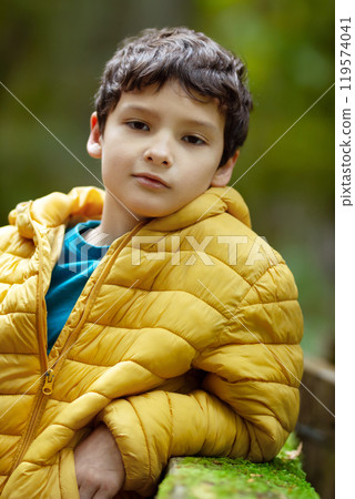 Portrait of a boy in yellow jacket leaning on a mossy wooden fence during his strip to a rainforest. Cathedral grove, Vancouver island, British Columbia, Canada. Portrait of a boy in yellow jacket leaning on a mossy wooden fence during his strip to a rainforest. Cathedral grove, Vancouver island, British Columbia, Canada. 119574041