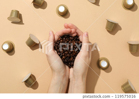 Golden coffee capsules and coffee bean in hand on beige background, top view Golden coffee capsules and coffee bean in hand on beige background, top view 119575016
