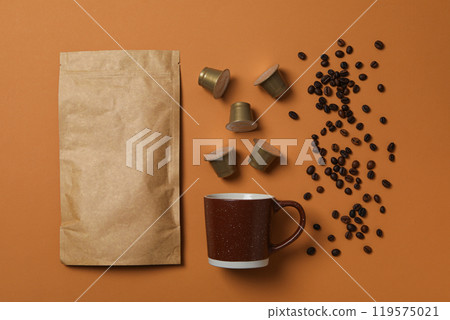Coffee capsules and beans, cup, paper bag on brown background, top view Coffee capsules and beans, cup, paper bag on brown background, top view 119575021
