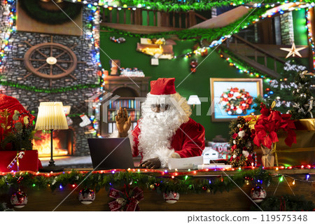 African american Santa Claus chatting with parents and kids before Christmas, gathering wishes for toys as gifts. Modern Saint Nicholas using technology to make children happy, holiday spirit. 119575348