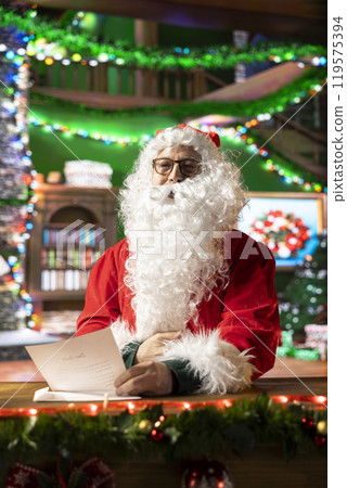 Santa Claus reading a letter in his cozy festive decorated workshop. Letters to Father Christmas filled with wishes and childhood magic during the holiday season, x mas tradition. Santa Claus reading a letter in his cozy festive decorated workshop. Letters to Father Christmas filled with wishes and childhood magic during the holiday season, x mas tradition. 119575394