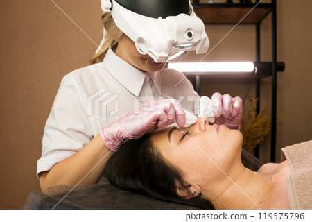 Beautician meticulously wipes client's forehead using soft pads 119575796