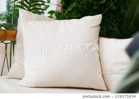 A Cozy White Pillow Placed on a Stylish Sofa, Beautifully Surrounded by Lush Green Plants 119575834