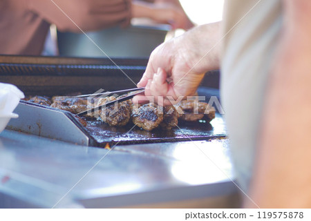Grilling Delicacies A Skilled Chef Cooking Delicious Burgers on a Charcoal BBQ Grill 119575878