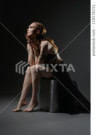 A thoughtful woman in a black outfit sits gracefully on a stool in the studio 119576152