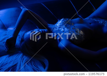 Elegant model reclining on a couch surrounded by blue lighting at night 119576173