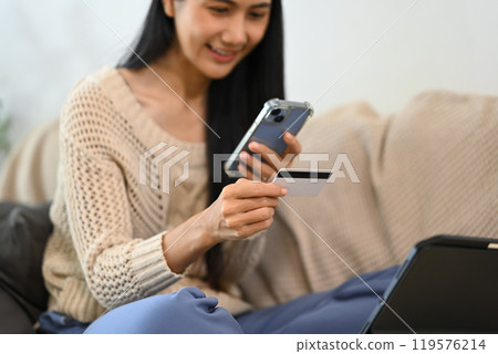 Happy young woman using credit card for online shopping on her smartphone Happy young woman using credit card for online shopping on her smartphone 119576214