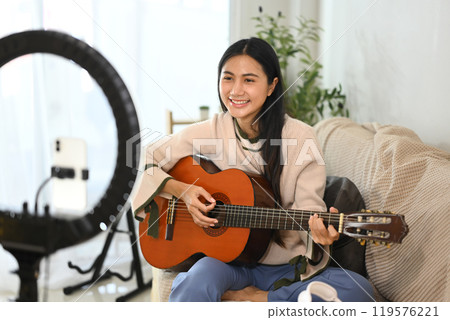 Smiling young woman live streaming a guitar performance from home 119576221