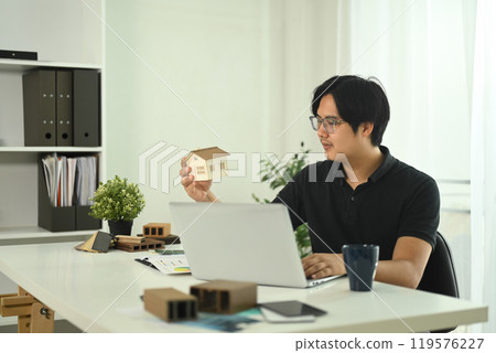 Professional architect holding house model while reviewing design plans in office 119576227