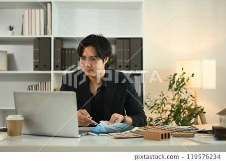 Architect using laptop and reviewing color samples for a project at his office 119576234