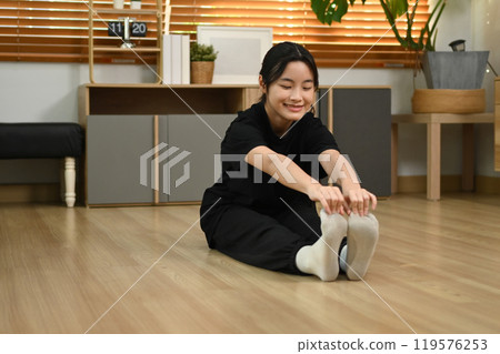 Smiling asian girl stretching her legs on floor getting ready for workout at home 119576253