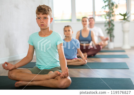 Calm preteen boy practicing lotus pose of yoga with his family Calm preteen boy practicing lotus pose of yoga with his family 119576827