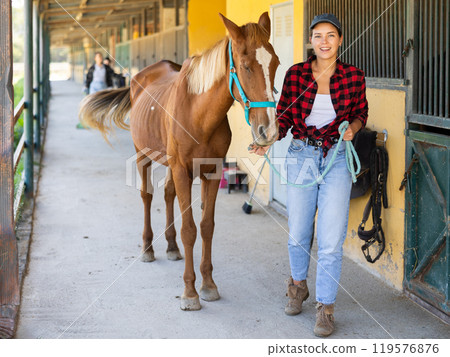 Young woman leads horse out of stable Young woman leads horse out of stable 119576876