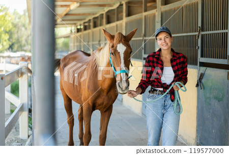 Young woman leads horse out of stable 119577000