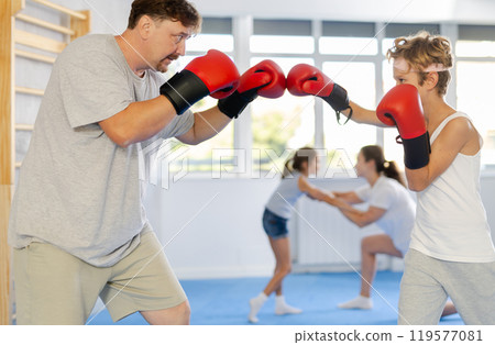 Boy and dad are boxing in gym, father helps child to work out force of blow. Boy and dad are boxing in gym, father helps child to work out force of blow. 119577081
