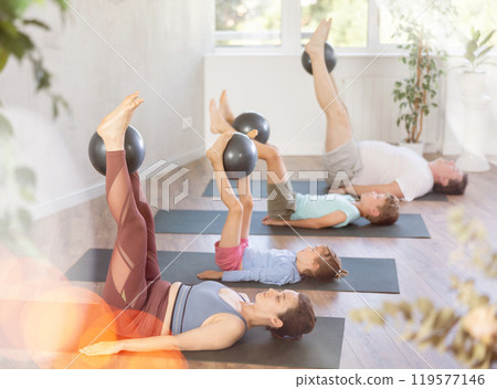 Family with two children doing yoga and pilates using soft ball in gym 119577146
